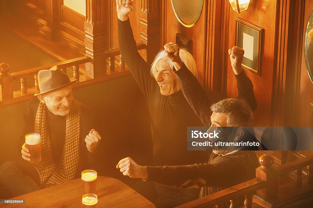 Friends in a pub Group of friends  enjoying in beer.They watch a football game, cheering in the old pub. The grain and texture added. Very shallow DOF . Active Seniors Stock Photo