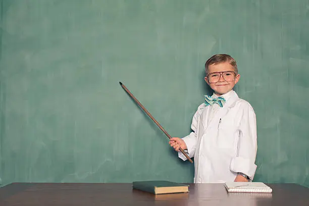 Photo of Young Boy Dressed as Scientist Points to Chalkboard