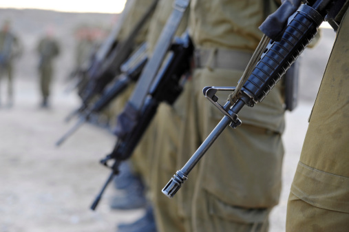 Israeli soldiers forming wearing IDF uniforms an L shape. Selective focus on a front gun barrel of an M-16A4 assault rifle.