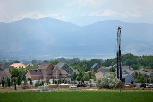 Just off Interstate Highway 25, Drill Rig 1548 - Encana Natural Gas, works closely with their fracking drill rig in front of homes in the town of Frederick in Weld County, Colorado. Pipes, vehicles and storage tanks also stand in front of homes as hazy, snow capped front range of the Rocky Mountains stand in the background.