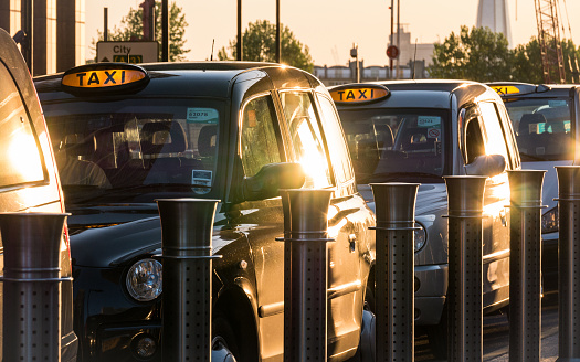 London, UK - 13 May 2015: A dusk scene of a row of familiar London black taxi cabs lined up at a taxi rank waiting for passengers in Docklands, London's business and finance district.