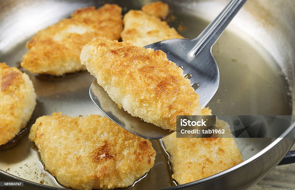 Golden Fried Fish in Pan Horizontal photo of golden breaded coated fish being fried in stainless steel frying pan with focus on single piece with spatula underneath Deep Fried Stock Photo