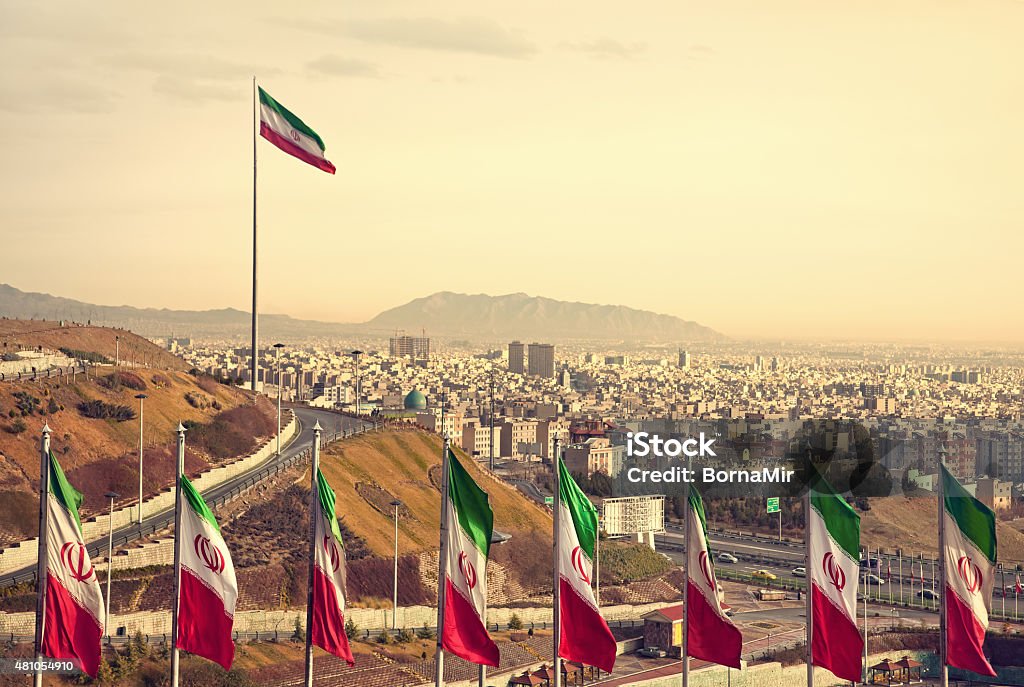 Row of Iran Flags in Front of Tehran Skyline Set of Iran flags in Front of Tehran Skyline and one large flag in the background at sunset with orange warm tone. Iran Stock Photo