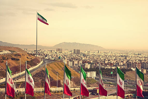 Row of Iran Flags in Front of Tehran Skyline Set of Iran flags in Front of Tehran Skyline and one large flag in the background at sunset with orange warm tone. iran stock pictures, royalty-free photos & images