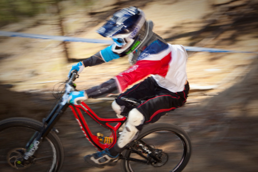 Spokane, Washington USA - March 23, 2014: A racer becomes a blur of motion as he passes by on his run on a downhill mountain bike course. He is fully outfitted with a full face helmet, knee protectors, and other body armor in case of a crash.