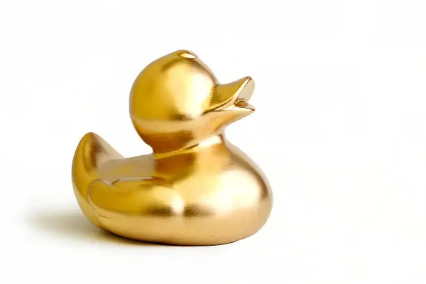 A gold rubber ducky toy on a white background with slight shadow.