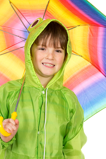 A seven year old boy in a green raincoat with a rainbow coloured umbrella, isolated on white.