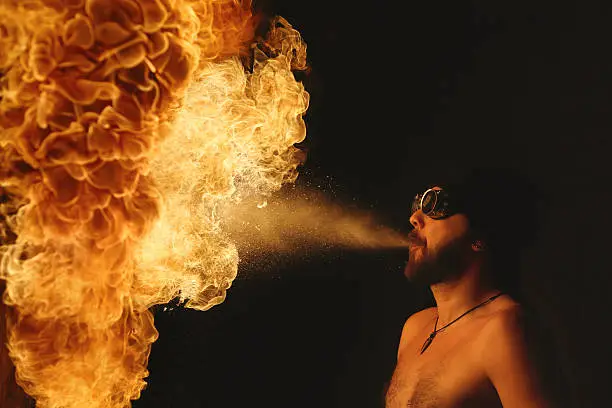 Fire breather blowing a fire ball from his mouth.