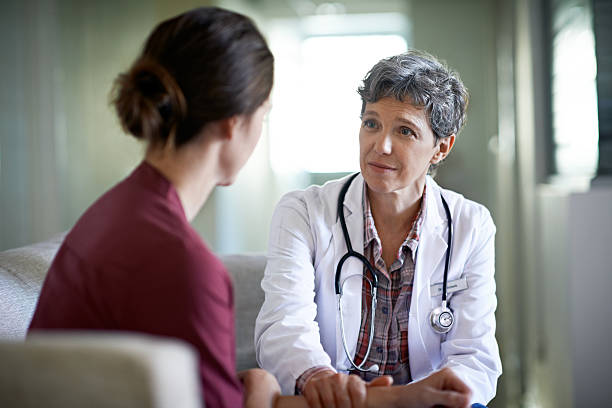 I know this is difficult news Shot of a compassionate doctor comforting a young woman in a hospital waiting room woman talking to doctor stock pictures, royalty-free photos & images