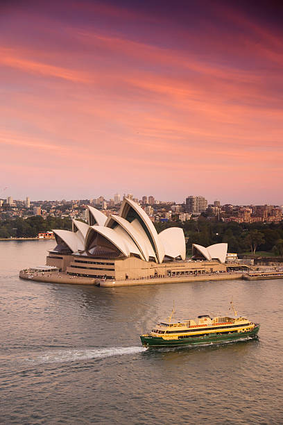 Sydney, Australia - March 18, 2014: A Manly ferry passes the Sydney Opera House, underneath pink and orange clouds at sunset.