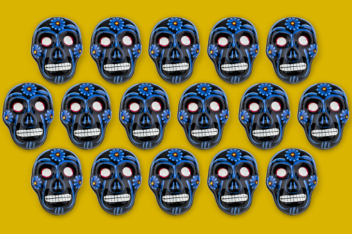 Multiply hand painted Mexican skulls on top of yellow background.