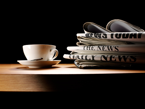 Pile of newspapers and a coffee cup on a table.