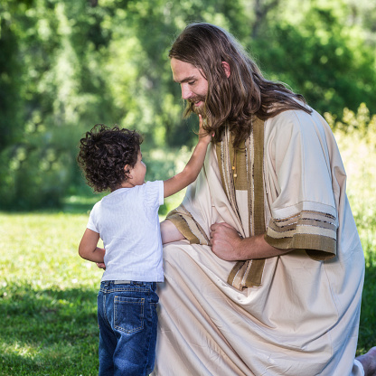 Jesus Christ is calm and serene - smiling and kneeling down in front of a small three year old Hispanic boy so the child can gently touch his beard. June 2015 Utah USA War and Peace photo shoot.