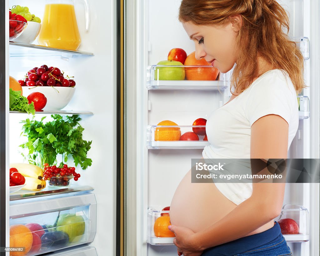 nutrition and diet during pregnancy. Pregnant woman with fruits nutrition and diet during pregnancy. Pregnant woman standing near refrigerator with fruits and vegetables Pregnant Stock Photo