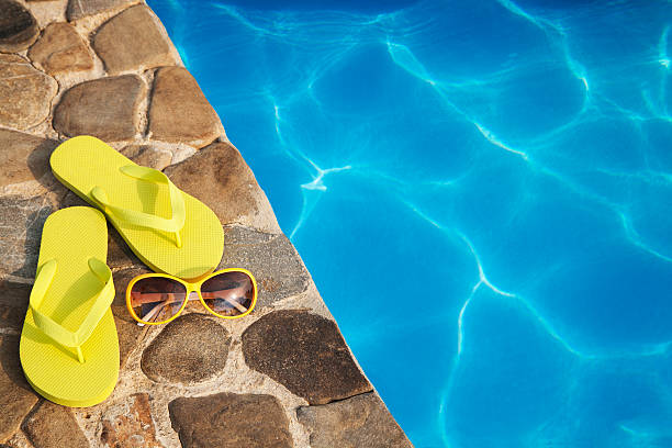 istock Yellow slippers and sunglasses by a swimming pool 481086506