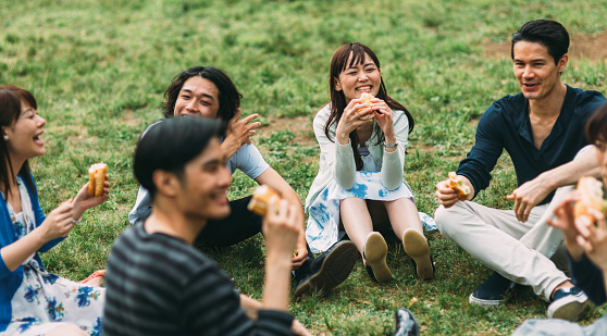 Japanese teenagers eating some fast food outside in the park. There is a lovely sunny day. The food seem delicious and they seem satisfied.