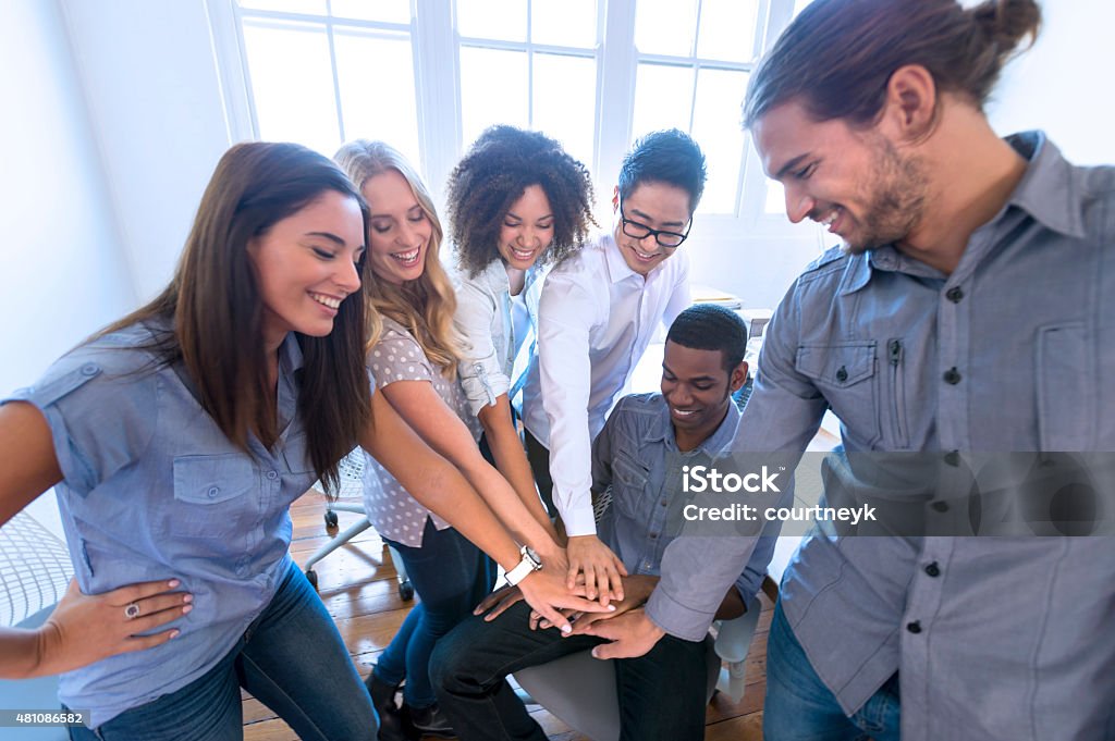 Group of young multi cultural business people celebrating. Group of young multi cultural business people celebrating. They are all excited and very happy. Looks like they have just won a big contract. All have their hands together showing cooperation, bonding and support. They are casually dressed in a modern office. Several ethnic groups are represented including Caucasian, African American, and Asian. Holding Hands Stock Photo