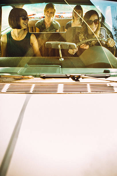A group of young women laugh and have fun on a road trip adventure in a classic car. Vertical image with copy space.