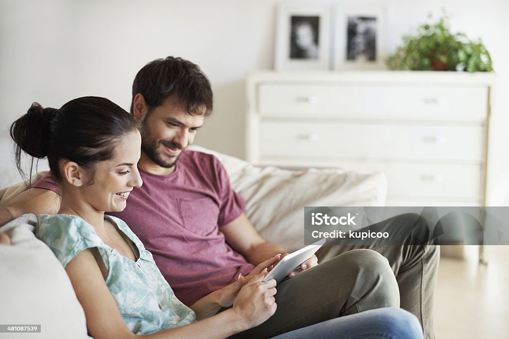Showing him something she saw online A young couple sharing their tablet while relaxing on the sofa Adult Stock Photo