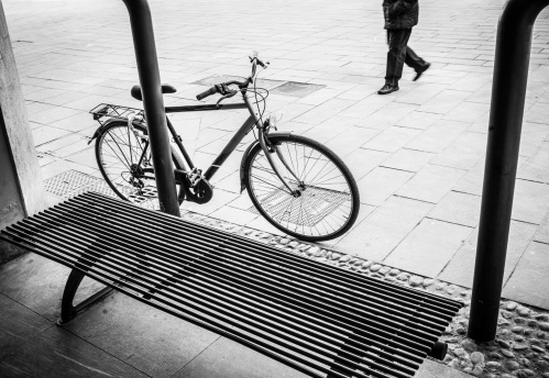 Bicycle leaning close to metal bench. Black and white.