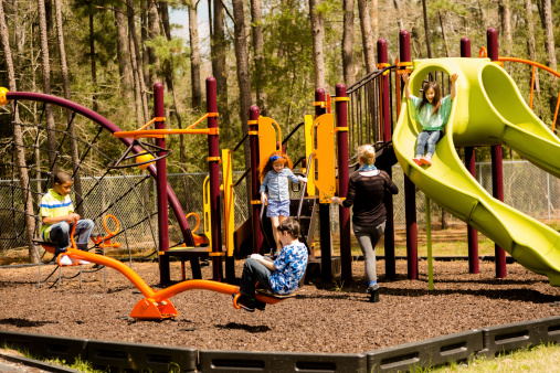 Elementary age children play during school recess or at a park setting. Playground equipment, slide, see saw.  Teacher or mom checks on children.