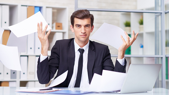 Self-confident young businessman throwing away papers at office