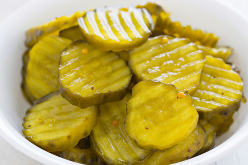 A high angle close up shot of a bowl full of bread & Butter chips pickles.