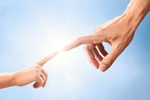 Close up of two hands, adult's and childâs, reaching each other like Michelangelo's painting in front of sun and bright blue sky.