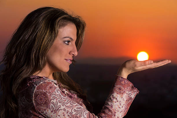 Beautiful young woman , watching sunset, holding sun in hand