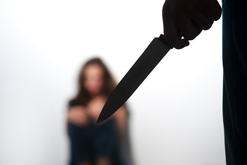 Close up of man's hand holding knife, scared woman in background