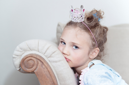 Germany, Bavaria, Little Princess on a vintage chair, sad 6 year old blond girl dresses like a princess Little Princess on a vintage chair, sad 6 year old blond girl dresses like a princess