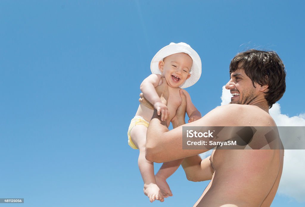 Father and son playing on the beach Beautiful young father picked up his son up in the air. They are on the beach. Sky is behind them. Playing time. Baby - Human Age Stock Photo