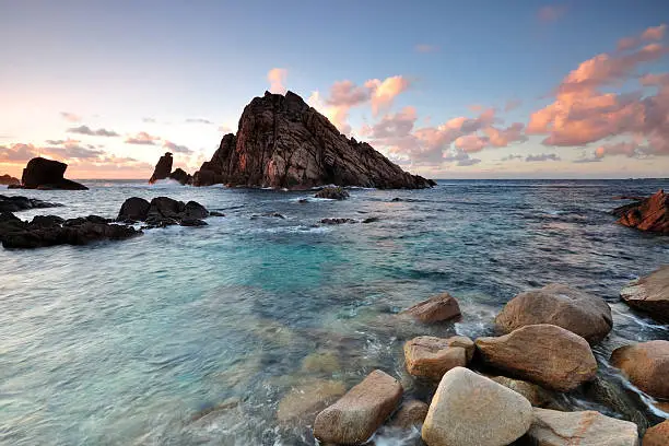 Summer Sunset in Sugarloaf Rock, Cape Naturaliste, Western Australia. Pink and blue sky with plants and grass on a foreground. Triangle-shaped Sugarloaf Rock rises dramatically up out of the ocean along the coast between Yallingup and Cape Naturaliste.  