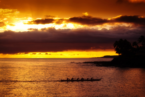 A traditional outrigger canoe boat in the tropical seas of Hawaii at sunset.