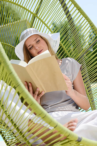istock cheerful young blond woman reading relaxed swing by the pool 481129576