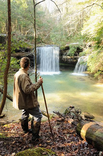 istock Man hiking in woods by waterfall into pond 481129929