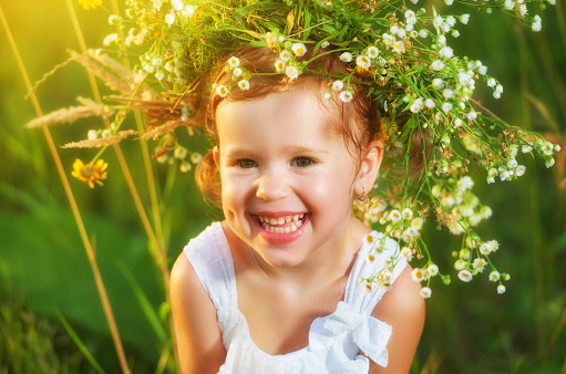 funny happy baby child girl in a wreath on the nature laughing in a meadow in summer