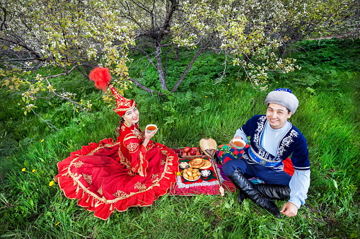 Kazakh couple drinking tea on the green grass in apple garden of Almaty, Kazakhstan, Central Asia