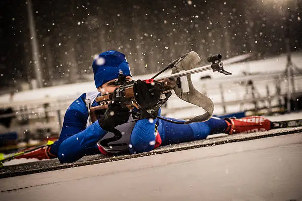 Athletic man lying on deck and ready to fire biathlon rifle.