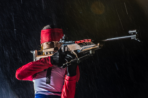 Athletic woman holding biathlon rifle to fire and her finger on trigger.