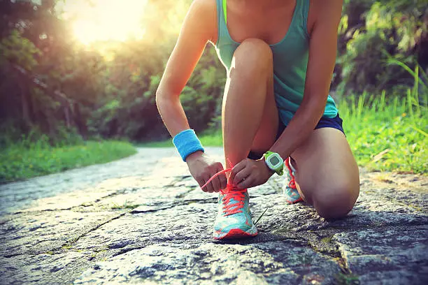 Photo of young woman runner tying shoelaces on stone trail