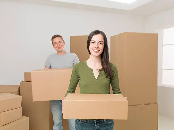 young happy couple carrying cardboard boxes, moving house