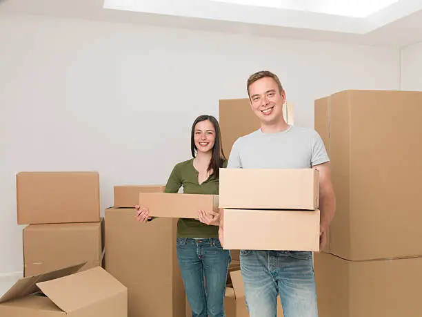 young happy couple carrying cardboard boxes, moving house