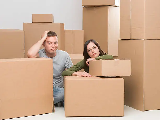 couple sitting around cardboard moving boxes, sad about leaving their home