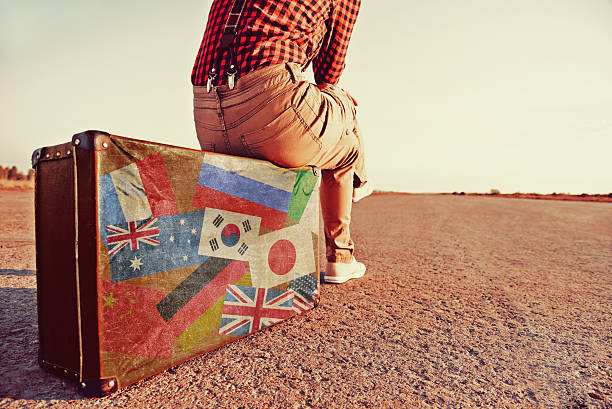 Tourist woman sitting on a suitcase on road. Suitcase with stamps flags of different countries. Concept of travel