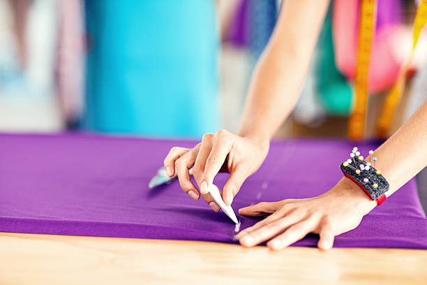 Cropped image of female designer measuring textile with chalk in fashion studio. Horizontal shot.