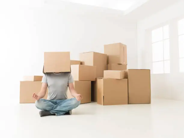 man sitting on floor in new apartment, meditating with box on his head