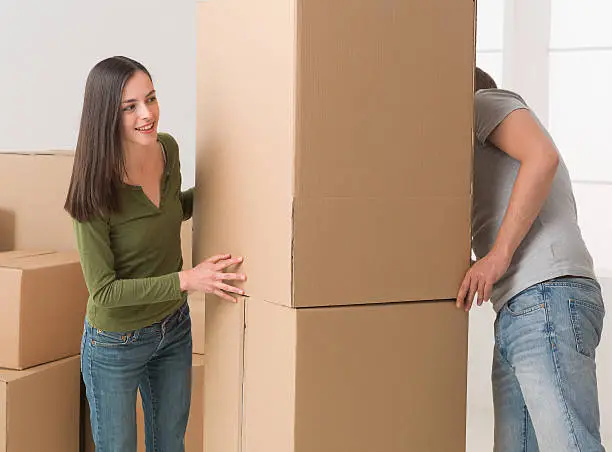 young couple playing hide and seek around cardboard boxes while moving house