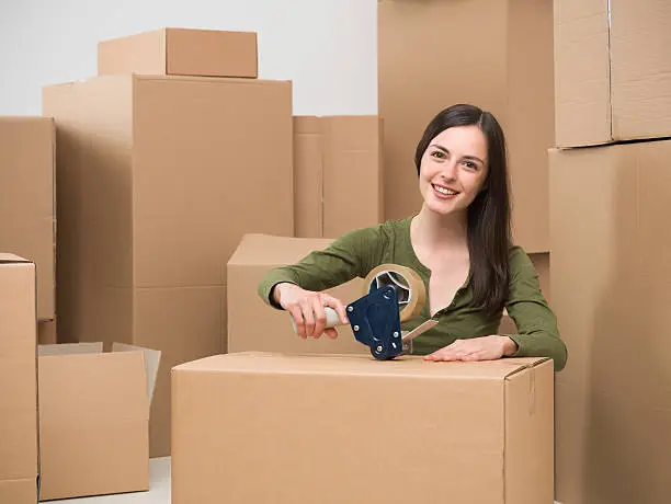 young caucasian woman sealing a cardboard box with adhesive tape. moving home