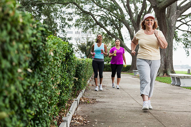 Women exercising in park Multi-ethnic women exercising in park, power walking.  Focus on senior woman (60s) in foreground. racewalking photos stock pictures, royalty-free photos & images